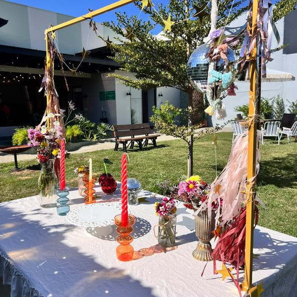 Mesa de festa no jardim com arco dourado e velas coloridas